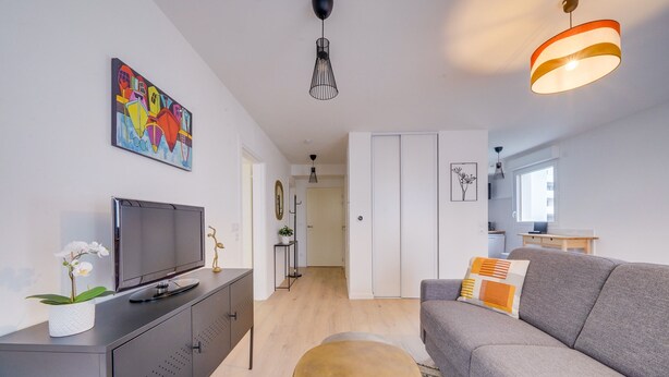 Un soggiorno moderno con un divano grigio, un tavolino rotondo, una TV su un mobile e un quadro colorato appeso al muro.