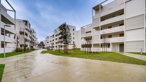 Un edificio residenziale moderno con diversi balconi, un cortile centrale alberato e un marciapiede bagnato.