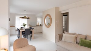 Una sala de estar moderna con un sofá color beige, un espejo redondo y un comedor con mesa y sillas.