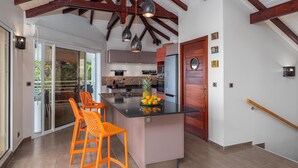 A modern kitchen with a central island, orange bar stools, and a wooden door.