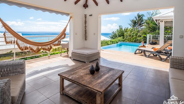 A spacious patio with a view of the ocean, a hammock, a pool, and outdoor seating.