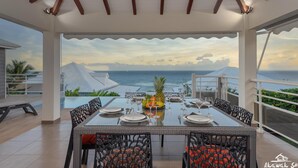 A dining area with a table set for six, overlooking a scenic ocean view.