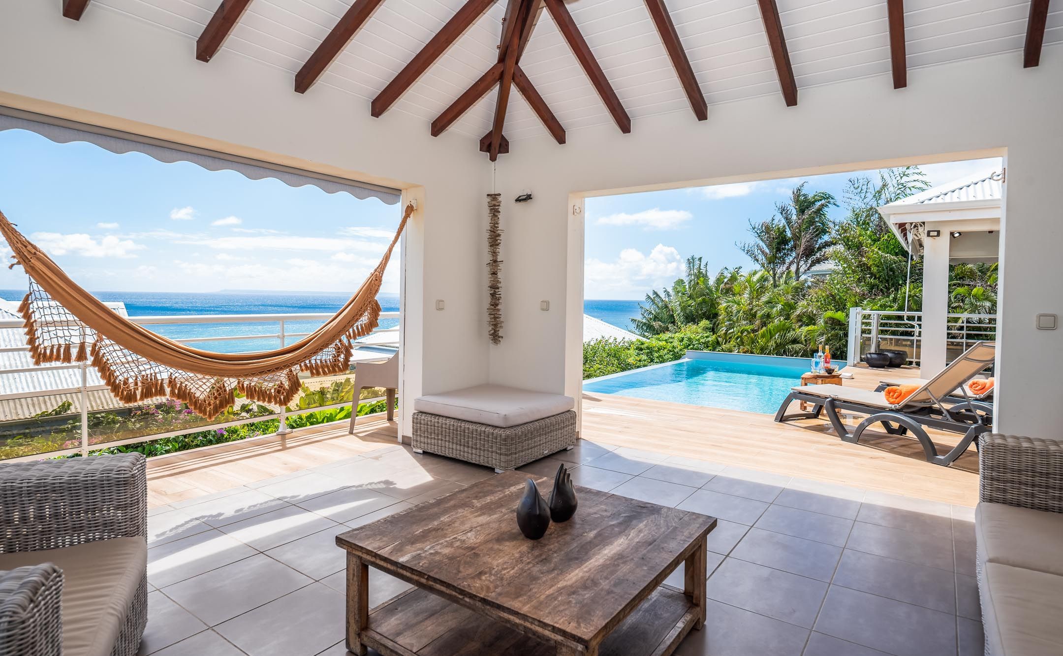 A spacious patio with a view of the ocean, a hammock, a pool, and outdoor seating.