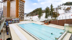 En swimmingpool med utsikt över en hög byggnad och en skidbacke i bakgrunden.