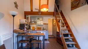 Une cuisine compacte dotée d’un îlot central, d’un escalier en bois et d’un coin repas avec des tabourets.