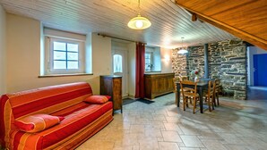 Una habitación acogedora con techo de madera, un sofá rojo a rayas, una mesa de comedor con sillas, una pared de piedra y una ventana con cortinas.