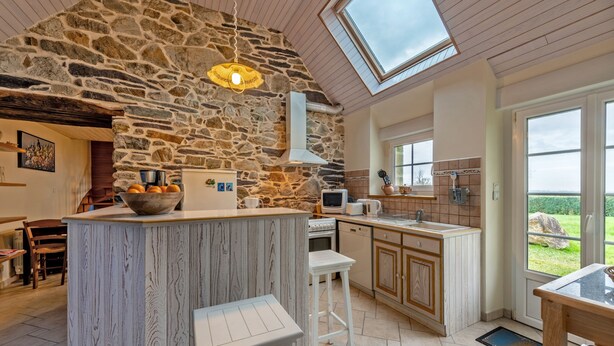 Una cocina con pared de piedra, techo de madera y tragaluz.