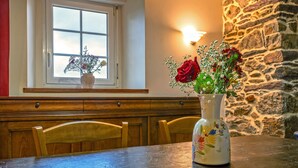 Una mesa de comedor con un florero, sillas de madera, una ventana con vistas y una pared de piedra.