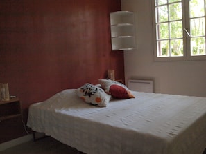 A bedroom with a bed, pillows, a bedside table, a window, and a wall-mounted light fixture. - Cantebos - Maison avec 3800 m² de jardin (Saint-Laurent-Médoc)