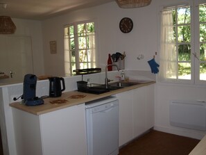 A kitchen with a coffee maker, a dishwasher, a sink, and a clock on the wall.
