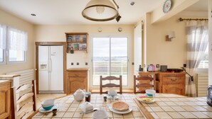 A kitchen with a dining table set for four, a refrigerator, a wooden cabinet, and a view through the glass door.