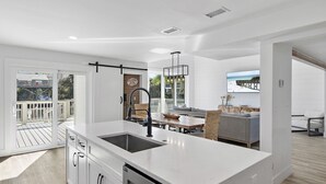 Une cuisine moderne dotée d’un grand îlot central, de portes-fenêtres coulissantes donnant sur une terrasse et d’un coin repas offrant une vue sur l’océan.