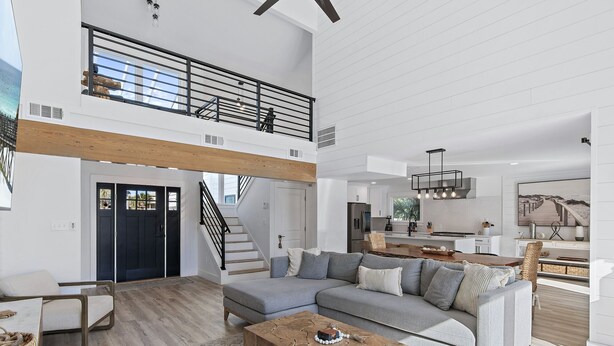 Un vaste espace de vie comprenant un grand canapé d’angle gris, une table basse en bois et un escalier menant à une mezzanine.