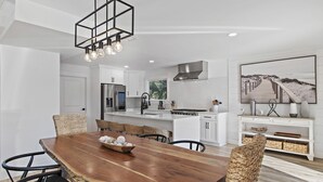 Une cuisine moderne avec des meubles blancs, un réfrigérateur en acier inoxydable et un luminaire suspendu.