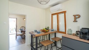 Une cuisine avec une table en bois, deux tabourets de bar, une machine à café et un panier de fruits.