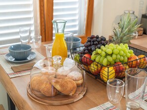 Colazione con croissant, cestino di frutta e bicchiere di succo d'arancia su un tavolo di legno.