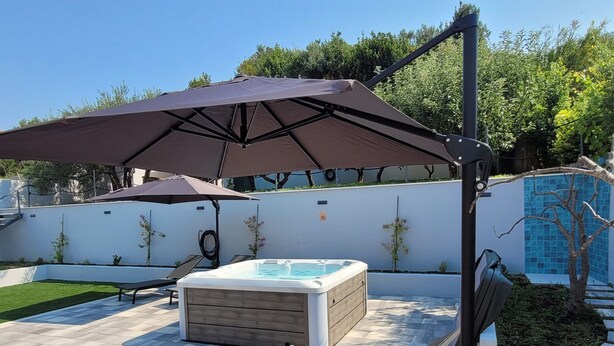 Un jardin avec un jacuzzi, deux chaises longues et un parasol.