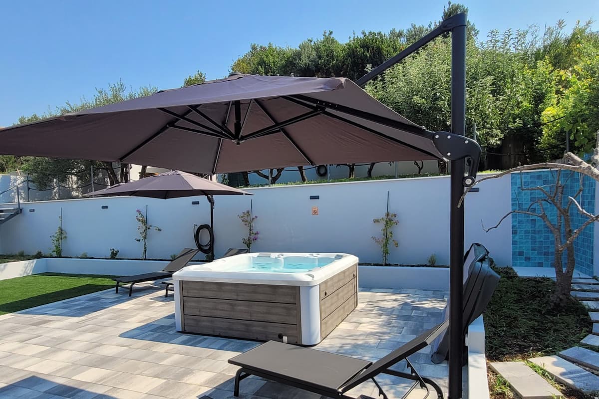 Un patio trasero con un jacuzzi, dos sillones de descanso y una sombrilla.