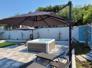 Een achtertuin met een jacuzzi, twee loungestoelen en een zonnescherm.