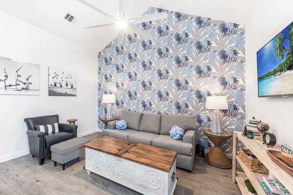 Een moderne woonkamer met een grijze bank, een zwarte fauteuil, een houten salontafel en behang met een patroon.