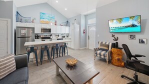 A modern kitchen with white cabinets, a central island, and a dining area with a wooden table. - Pet-Friendly Coastal Stay | Pools & Waterfront Access (Corpus Christi)