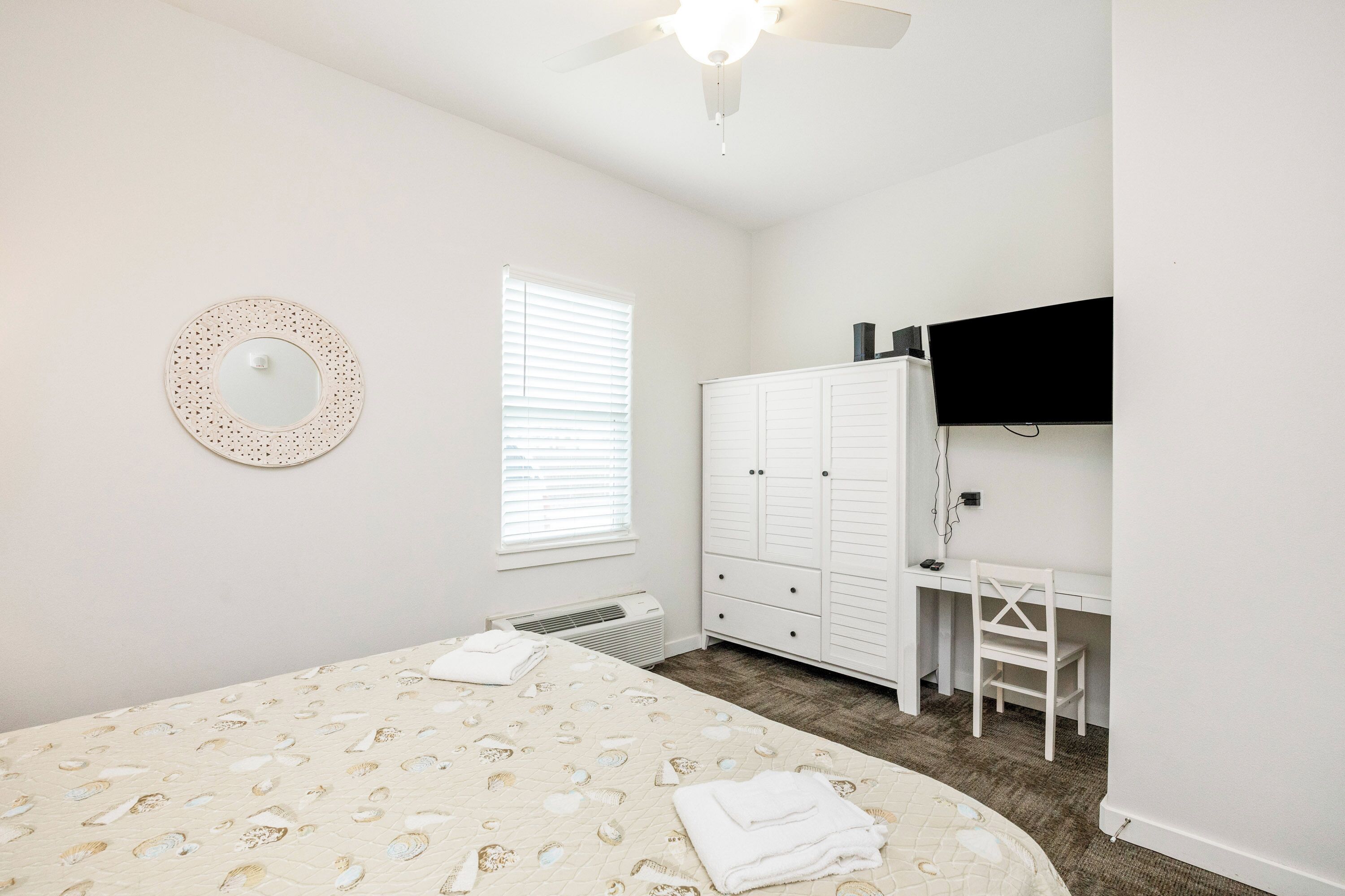 A bedroom with a bed, a wardrobe, a desk, and a ceiling fan.