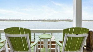 Eine Terrasse mit zwei grünen Adirondack-Stühlen und einem kleinen runden Tisch, mit Blick auf ein Gewässer und eine entfernte Uferlinie.