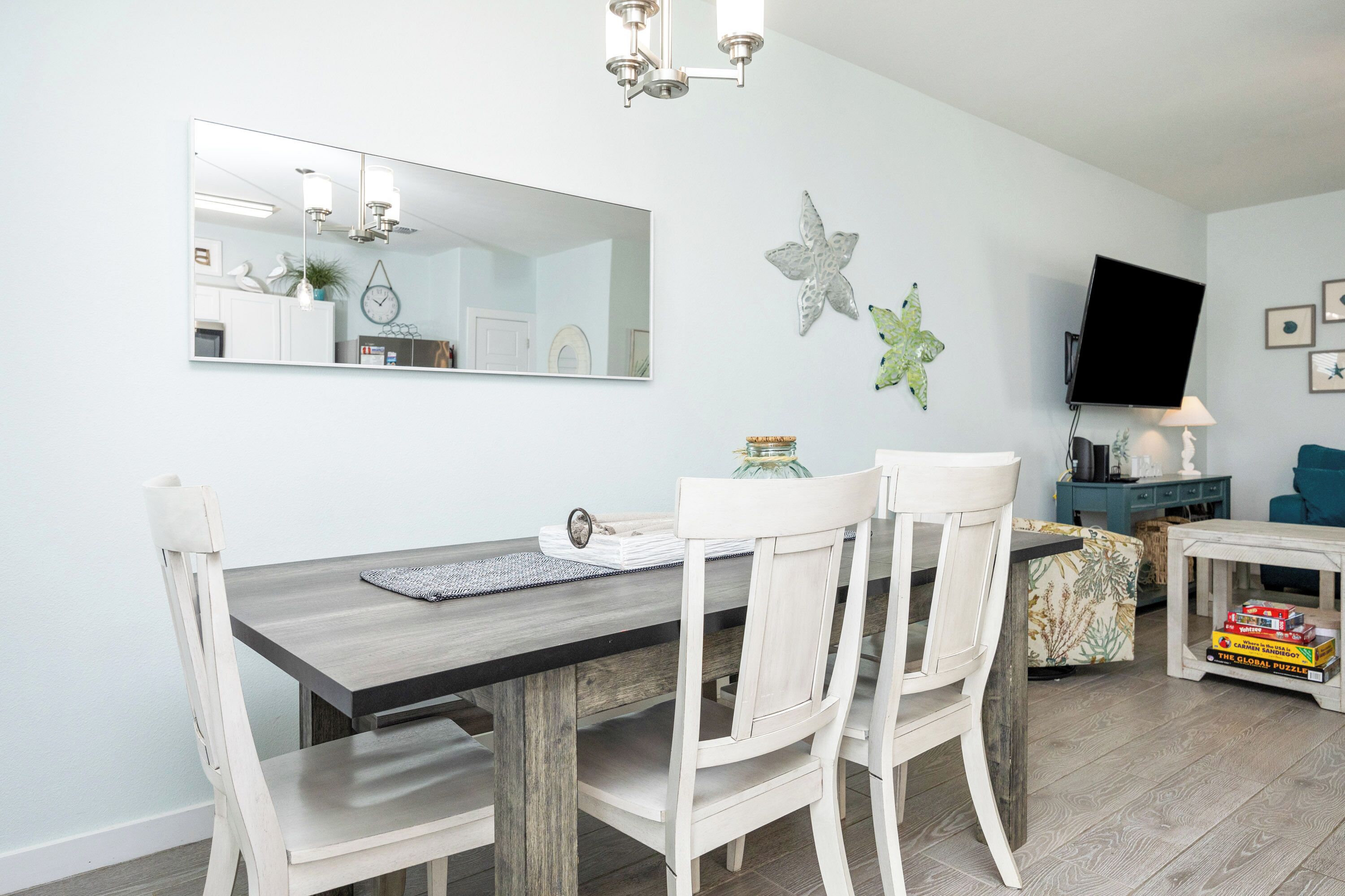 A dining area with a wooden table, white chairs, a mirror, and decorative items on the wall.
