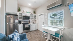 A compact kitchen with a refrigerator, microwave, and oven, a dining area with a table and chairs, and a window with blinds. - Family Getaway | Swim, Slide & Relax w/ Pools & Splash Pad (Corpus Christi)