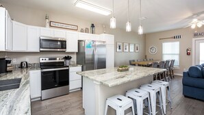A modern kitchen with white cabinetry, stainless steel appliances, and a central island with bar stools. - Serene Family Townhome | Water Views, Pools, Docks & Pets Welcome (Corpus christi)