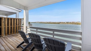 A wooden deck with Adirondack chairs overlooking a body of water and a distant shoreline. - Serene Family Townhome | Water Views, Pools, Docks & Pets Welcome (Corpus christi)