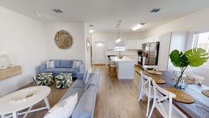 A modern living room with a blue sofa, a coffee table, and a dining area with white chairs and a wooden table.