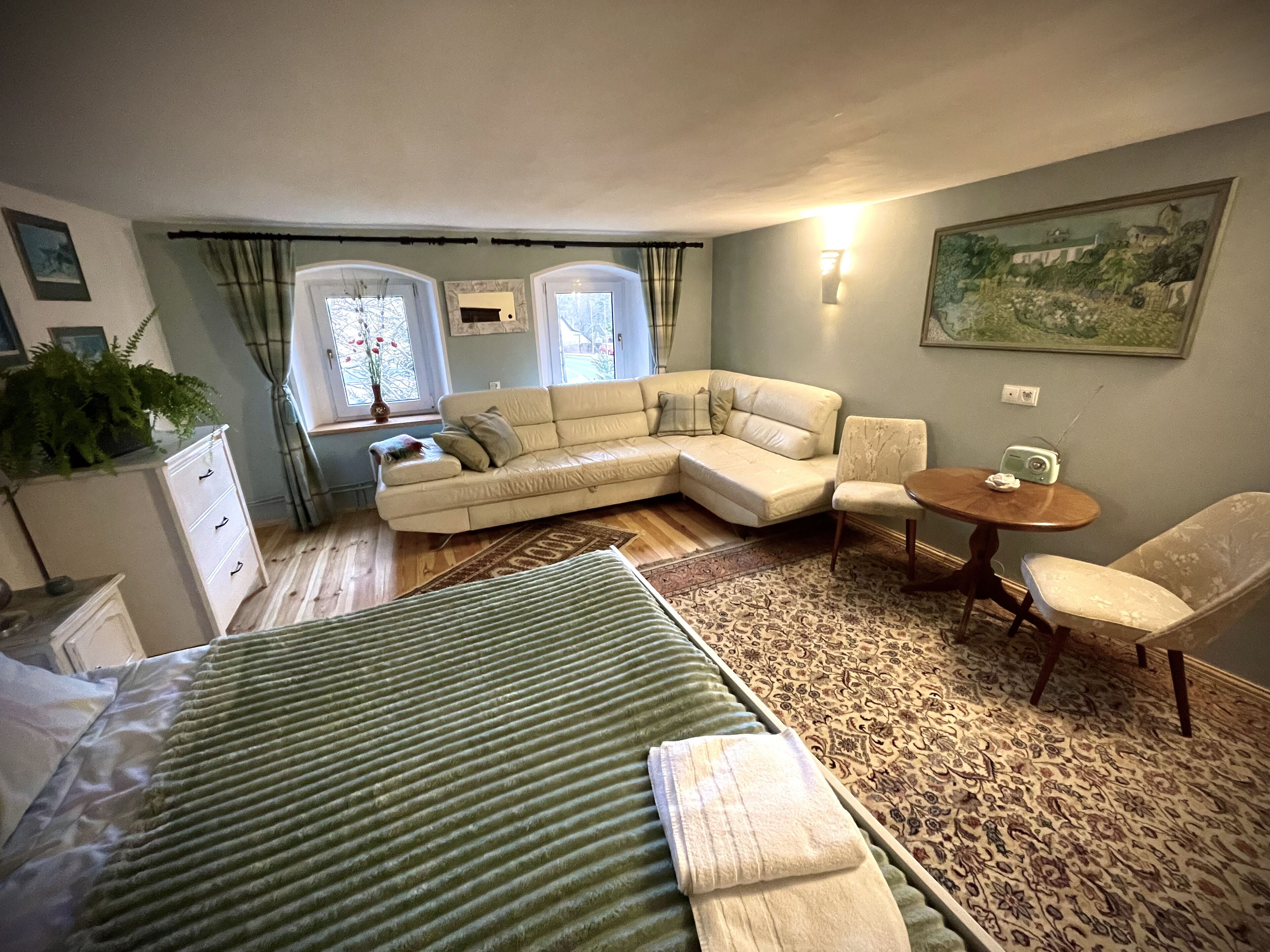Een slaapkamer met een bed, een bank, een stoel, een kleine tafel en een raam met gordijnen.