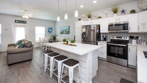 A modern kitchen with white cabinetry, stainless steel appliances, and a central island with bar stools.