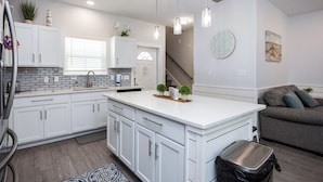 A modern kitchen with white cabinetry, a central island, pendant lighting, and a staircase leading to another level.