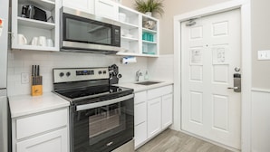 A modern kitchen with white cabinetry, a black stove, a microwave, and a sink. There is a plant on the countertop and a door with a lock and a light switch. - Endless Family Fun | Pools, Pickleball & Water Slides (Corpus Christi)