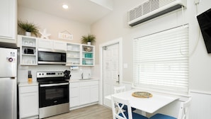 A modern kitchen with white cabinetry, a stainless steel stove, and a white dining table with blue cushioned chairs. - Endless Family Fun | Pools, Pickleball & Water Slides (Corpus Christi)