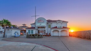 A waterfront property with a large house featuring a prominent sign, a garage, and a well-maintained lawn. - Coastal Escape | Resort Amenities, Pools & Pickleball (Corpus Christi)