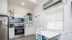A modern kitchen with white cabinetry, a built-in oven, and a dining area with a white table and blue chairs.