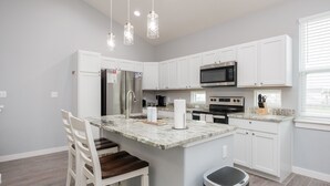 A modern kitchen with white cabinets, a marble island, stainless steel appliances, and pendant lighting.