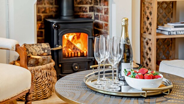 Une pièce chaleureuse avec une cheminée, une table sur laquelle se trouve un plateau avec des verres et une bouteille, et un bol de fraises.