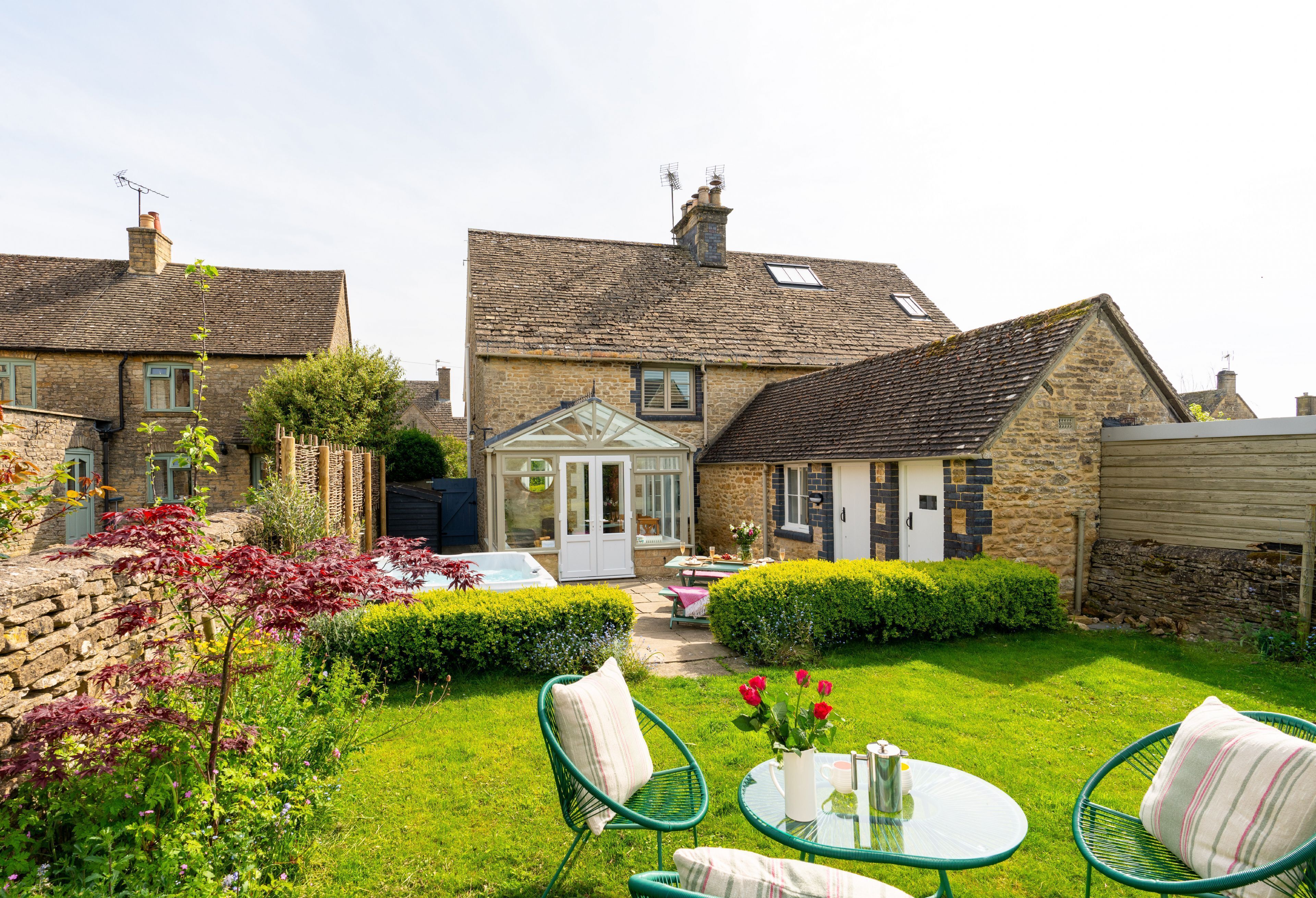 A traditional stone house with a well-maintained garden, a patio with chairs, and a conservatory.
