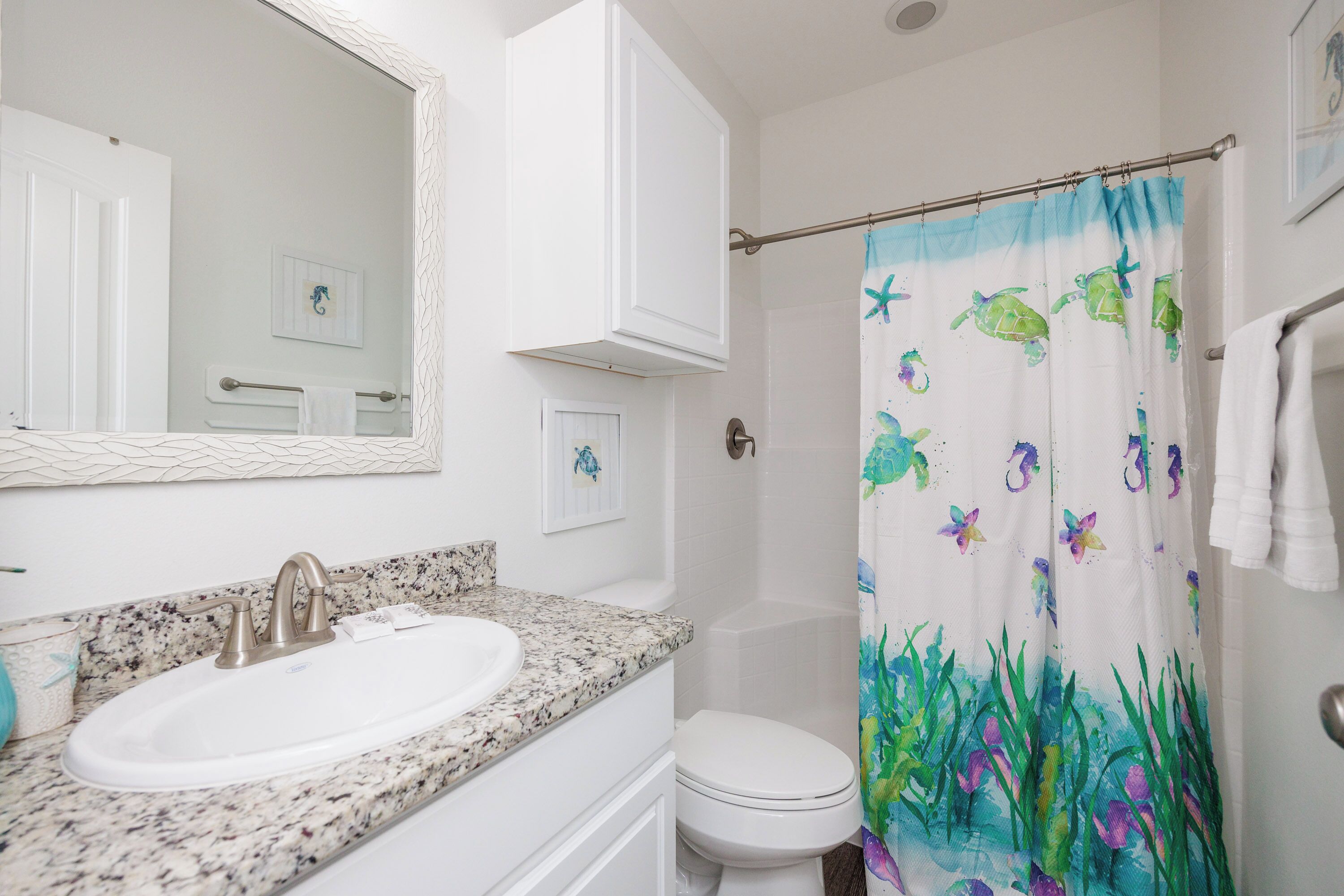 A bathroom with a white sink, a mirror, a shower curtain with sea turtle and plant designs, and a white toilet.