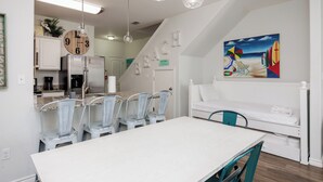 A modern kitchen with a dining area, a staircase leading to a loft bedroom, and a beach-themed painting. - Pet-Friendly Beach Escape | Pool Views & Private Patio (Corpus Christi)