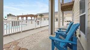 A covered outdoor area with a pool, white picket fence, and blue Adirondack chairs. - Pet-Friendly Beach Escape | Pool Views & Private Patio (Corpus Christi)