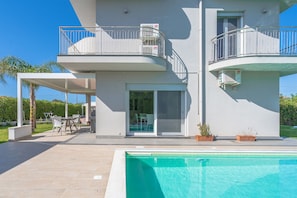 Et moderne hus med to etager, en balkon, en swimmingpool og en patio.