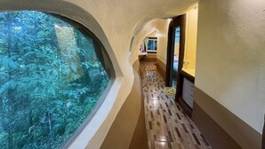 A hallway with a curved ceiling, a large window with a view of dense foliage, and a patterned floor.