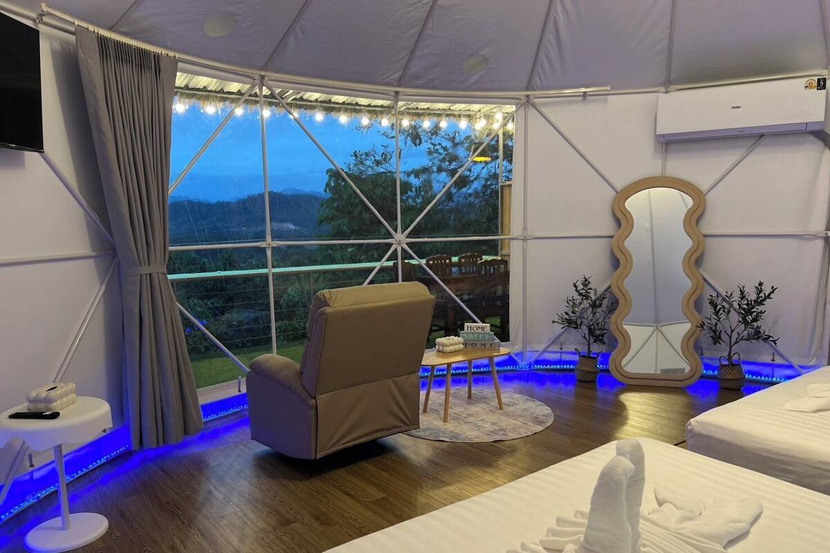 A tent-style room with a large window, a chair, a bed, a mirror, and a small table with a sign.