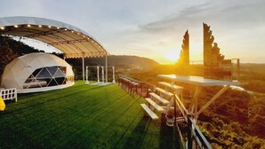 A tented event space with a grassy lawn and a scenic sunset view.