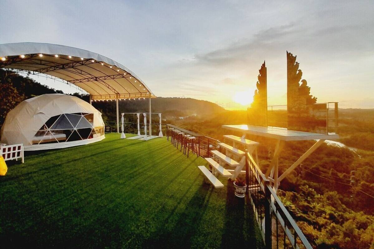 A tented event space with a grassy lawn and a scenic sunset view.